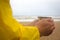Men in yellow raincoat on the beach over the stormy sea holding a cup of hot tea