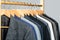 Mens suits in different colors hanging on hanger in a retail clothes store, close-up. Mens shirts, suit hanging on rack