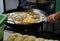 Merchant fries crispy yellow noodles on frying grate in hot oil big pan.