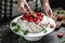 Meringue with whipped cream, fresh strawberrie and mint. Pastry chef in the kitchen decorating homemade Pavlova cake