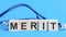 Merit word written on wooden blocks and stethoscope on light blue background