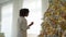 Merry Christmas. African American woman decorating Christmas tree. Happy girl near classical Christmas tree with white