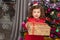 Merry Christmas. Cheerful beautiful little girl sitting near the Christmas tree holding a gift box. Christmas miracles. Happy New