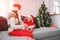 Merry Christmas and Happy New Year. Picture of happy kid sitting on sofa and hold white small round sweet. She looks at