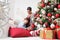 Merry christmas, happy pregnant woman and her child touch the belly near the illuminated and decorated tree with under wrapped