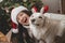 Merry Christmas! Happy woman in santa hat hugging funny white danish spitz dog in festive room. Cute dog in reindeer antlers