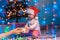 Merry Christmas. A little kid in a Christmas hat gets a gift. Festive lights and xmas spruce on the background. The