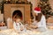 Merry Christmas! Mother and child girl with gifts at home, sitting on floor with crossed legs, being excited and happy, looking at