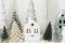 Merry Christmas! Stylish little Christmas trees and house decorations on white table. Modern christmas scene, miniature snowy