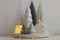 Merry Christmas! Stylish little Christmas trees and house on white table. Winter hygge, cozy christmas fairy scene, miniature