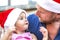 Merry christmas! young baby girl portrait celebrating xmas wearing a santa hat outdoor sitting on dad knees. father and child