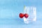 Merry. Red cherries hang on transparent glass. A ripe berry in a glass on a blue background.