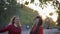 Merry smiling girls have fun jumping and spinning under fallen leaves in autumn park in fall season