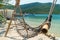 Mesh and bamboo hammock on a sandy beach and a yacht at sea in the tropics