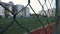 Mesh fence, close up. Unfocused football field behind mesh fence. View of people playing soccer on football field through grid