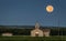 Mesmerizing shot of the full moonrise in a rural area and an old church in the foreground