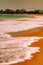 Mesmerizing vertical shot of the foamy white waves meeting the orange sand on the shoreline