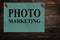 Messages `PHOTO MARKETING` written on green paper stands as an advertisement on a wooden surface