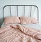 Messy bed with pink linen pillows, blanket and striped sheet