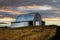 Metal barn in the field with yellow grass around and gloomy cloudy sky background at sunset