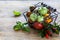 Metal basket with ripe different red, yellow and green tomatoes on a wooden table and basil leaves