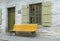 Metal bench in yellow. Facade of house with sash windows in green. White grainy wall Cobbled street. Canada