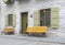 Metal benches in yellow. Facade of house with sash windows in green. White grainy wall Cobbled street. Canada