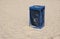 Metal blue garbage dustbin on beach sand