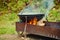 A metal boiler stands on a grill with fire and firewood, in a tourist Parking lot