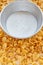 Metal bowl with milk on a painted white wooden background. Cornflakes scattered on a wooden table.