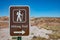 Metal brown sign with a white color walker informs the visitors that this area has a hiking trail. Petrified Forest, Arizona, US