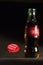 Metal cap with the inscription Coca-Cola falls in the air in front of a glass bottle on a dark background, color flare and glare;