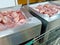 A metal cart next to the fresh pork in silver containers or shelves is on sale in the shopping mall or supermarket