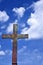 Metal cemetery cross against a blue sky with clouds