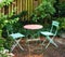 Metal chairs and table with blossoming plants in a park or private courtyard outdoors. Tranquil lush green landscape and