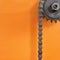 Metal cogwheel and black chain on orange background with empty space.