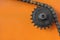 Metal cogwheel with chain on orange background.