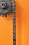 Metal cogwheel with chain on orange background closeup.