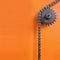 Metal cogwheel and chain on orange background with empty space.