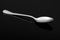 Metal dessert spoon on a reflective surface in black