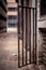 A metal doorway with padlock stands open in a dirty alleyway. Jo