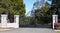 Metal driveway entrance gates set in brick fence with garden trees in background