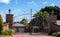 Metal driveway security entrance gates set in brick fence with residential garden in background against blue sky