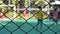 Metal fence against blurred background, close up. Unrecognized people playing football with fence in front. 4k