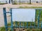 A metal fence with shabby paint and an empty white sign on the embankment, where people fish