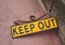 A metal fluorescent yellow keep out sign on a concrete floor with rusty chain attaching it to a wall with an iron hook