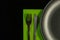 Metal fork, knife on green napkin and plate on a black background. top view on stainless knife and fork with copy space