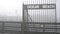 Metal gate of Ocean Beach pier in fog, misty boardwalk entrance California coast