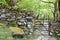 A metal gate through a stone wall leads to a rocky path into woodland