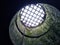 Metal grate covering a stone well with mossy walls leading to light and sky